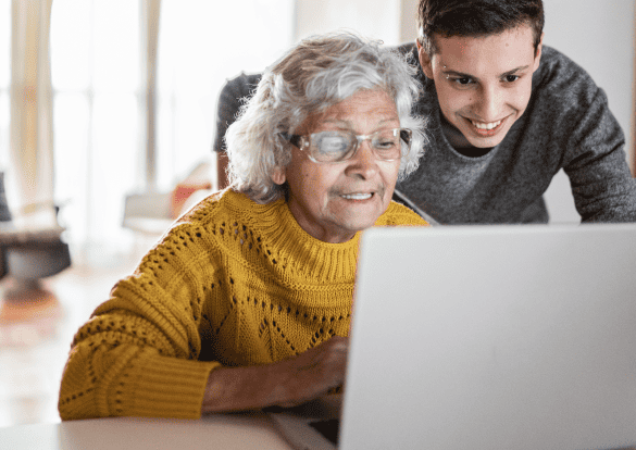 An elderly lady and her grandson look at the screen of an open laptop