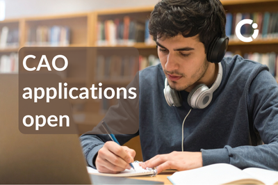 Student with headphones writing with pen next to his laptop. Text reads "CAO applications open".