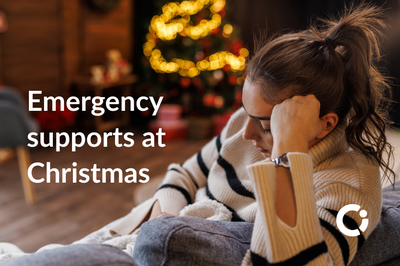 Young woman sits in thought on a couch with Christmas tree in background. Text reads: "Emergency supports at Christmas".